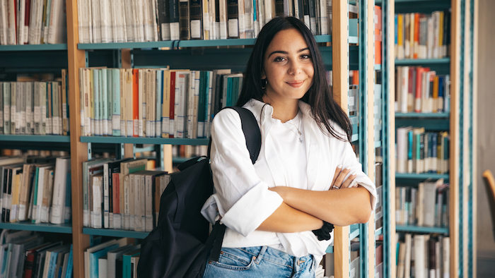College student leaning against bookshelf in campus library 