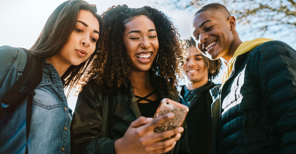 College student holding a phone in her hand surround by other students looking at the phone and smiling